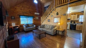 Interno di una baita in legno con soggiorno, divano, tavolino, scala e angolo cottura.