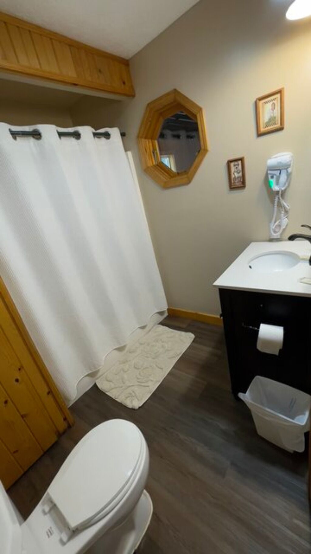 Un baño con inodoro, lavamanos, cortina de ducha, espejo y cubo de basura.