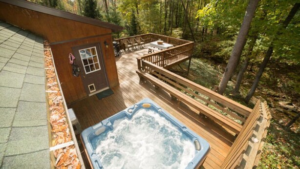 Una terrazza in legno con una vasca idromassaggio, circondata da alberi.