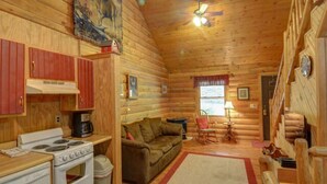 L’intérieur d’une cabane en rondins comprend une cuisine, un espace de vie avec un canapé et une table basse, ainsi qu’une fenêtre donnant sur un paysage agréable.