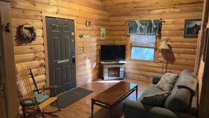 L’intérieur d’un chalet confortable, avec une cheminée, des murs en bois, un téléviseur, un canapé et un fauteuil à bascule.