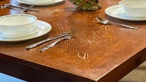 Une table de salle à manger en bois, mise avec de l’assiette blanche, des couverts en argent et une statuette d’ours décorative.