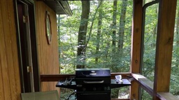 A wooden deck with a grill, a glass table, and chairs. - The Maple Tree Cabin (Bruceton Mills)