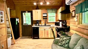 A cozy cabin-style kitchen with wooden cabinets, a sink, and a dining area with a table and chairs. - The Maple Tree Cabin (Bruceton Mills)