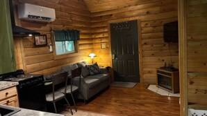 A cozy cabin interior with a kitchenette, a sofa, and a door. - The Maple Tree Cabin (Bruceton Mills)