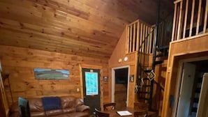 L’intérieur d’un chalet en bois comprend un coin repas, un salon avec un canapé et un escalier menant à un étage supérieur.