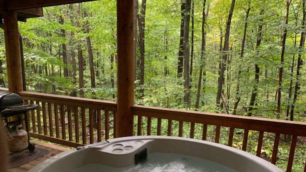 Un bain à remous avec une terrasse en bois et vue sur la forêt.