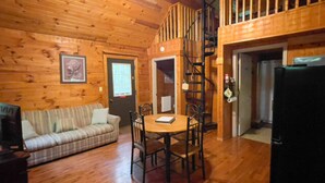 A wooden interior with a sofa, dining table, chairs, a staircase, and a refrigerator. - The Shawnee Cabin w/ Queen Bed (Bruceton Mills)