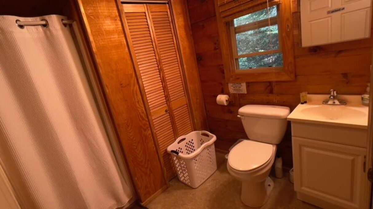 Een kleine, praktische badkamer met toilet, wastafel en een raam boven het toilet.