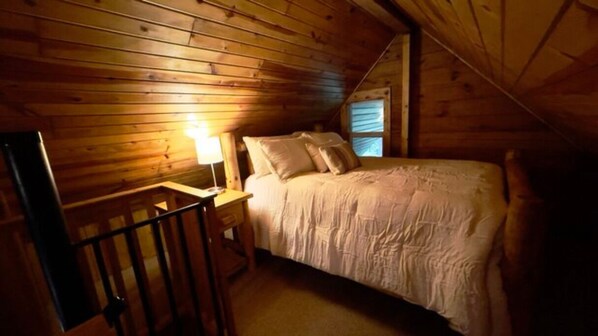 A wooden cabin bedroom with a bed, a nightstand, and a lamp.