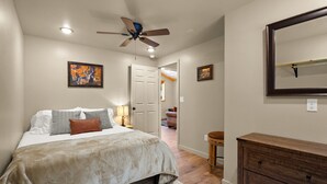 A bedroom with a bed, a ceiling fan, a dresser, and a door leading to another room. - Brand New Cozy Glacier Cabin (Coram)
