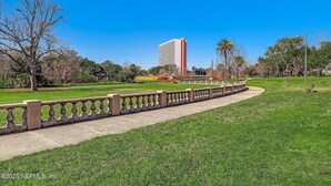 Un parque con un sendero pavimentado, un edificio alto al fondo y un cielo azul despejado.