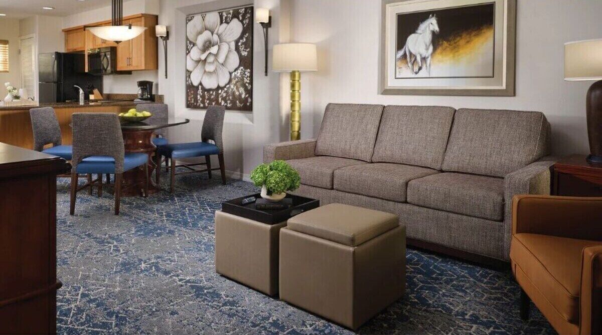 Ein modernes Wohnzimmer mit einer Couch, Hocker, einem Couchtisch und einem Essbereich mit Stühlen und einem Tisch.