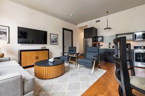 A modern living room with a sofa, armchairs, a coffee table, a flat-screen TV, a kitchen area with appliances, and a dining table. - 2BR Downtown Views in Prime Location The Mayfair (New Orleans)