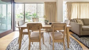 A modern living room with a dining area, featuring a large window with a view of high-rise buildings and greenery. - City & Palm View Oceanfront Bliss w/ Free Parking (Honolulu)
