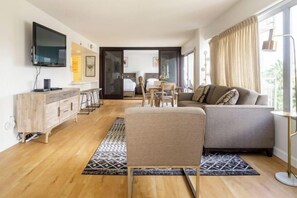 Una sala de estar moderna con un sofá, un televisor montado en la pared y una zona de comedor con mesa y sillas.