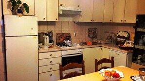 Una cocina compacta con gabinetes blancos, una estufa y una mesa de comedor con un frutero.