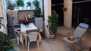 Un patio acogedor con una mesa y sillas, rodeado de plantas en macetas y un sillón colgante.