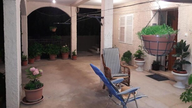 Un espacio al aire libre cubierto con plantas en macetas, una silla azul y jardineras colgantes.
