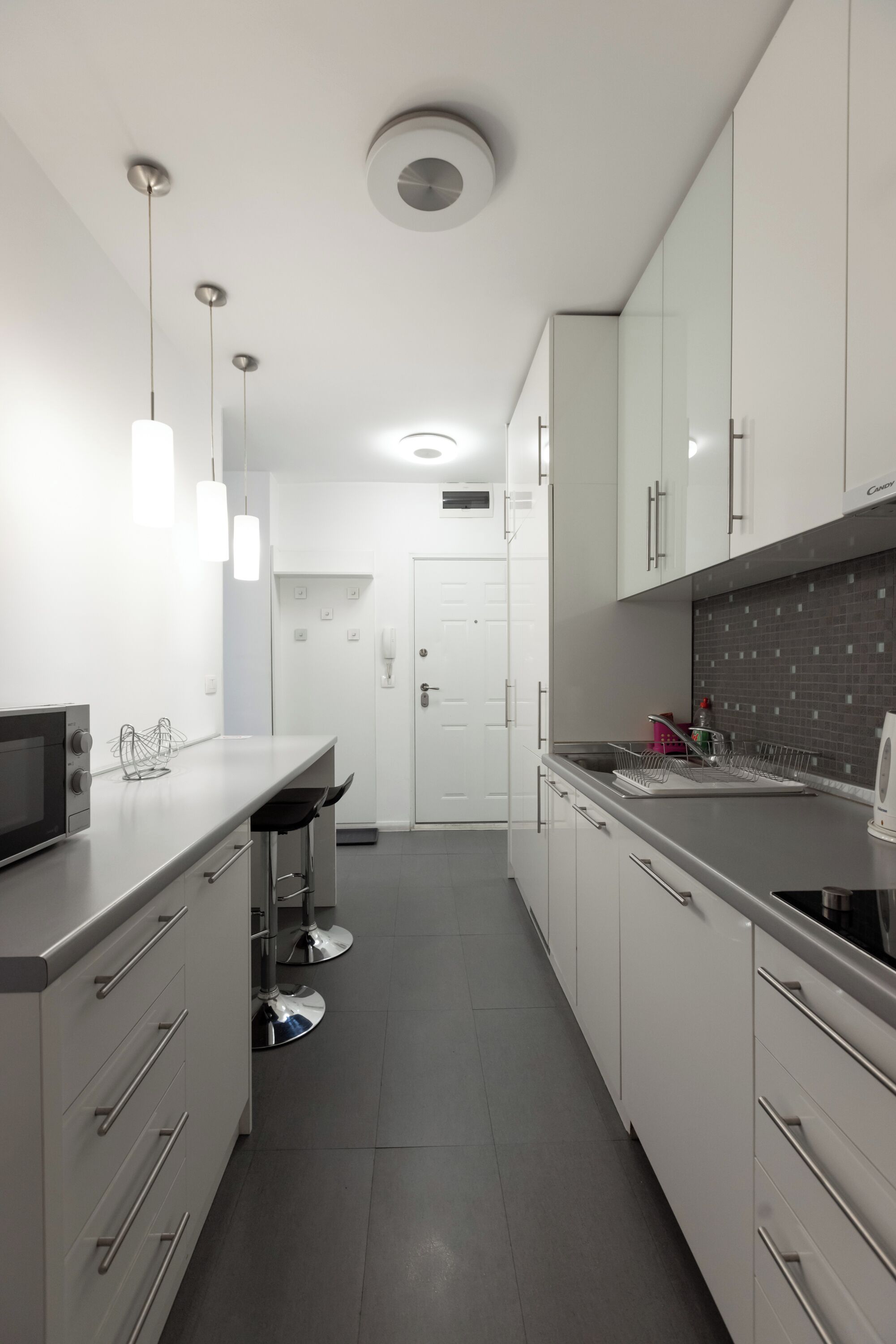 Una cocina moderna con gabinetes blancos, electrodomésticos de acero inoxidable e iluminación colgante.