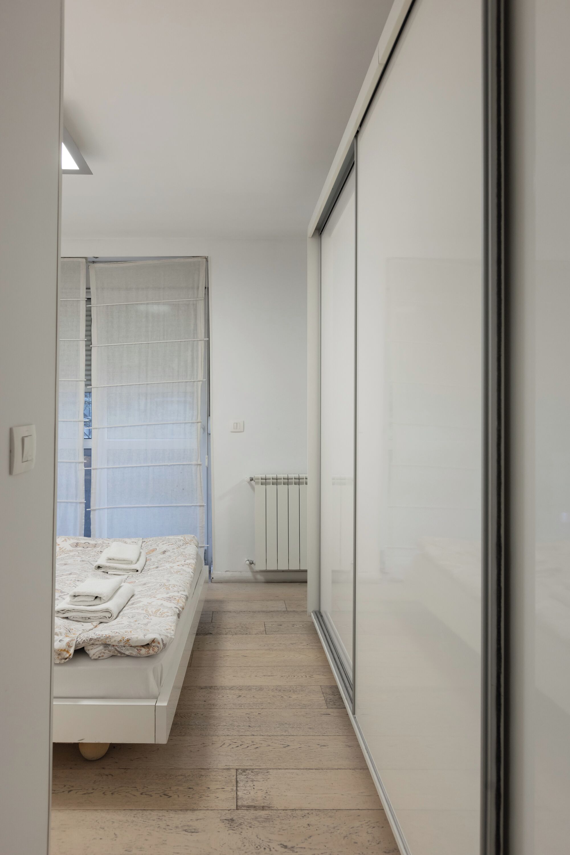 Un dormitorio moderno y estrecho, con una cama, un radiador y una puerta corredera.