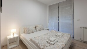 A bedroom with a bed, nightstand, and window with blinds. - Central Studio Apartments (Belgrade)