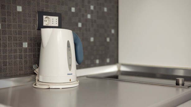 A white electric kettle on a kitchen countertop with a tiled backsplash. - Central Studio Apartments (Belgrade)
