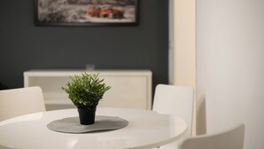 A round dining table with a potted plant in the center, white chairs around it, and a framed picture on the wall behind. - Central Studio Apartments (Belgrade)