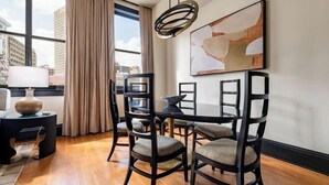 A dining area with a table and chairs, a lamp, and a painting on the wall. - 2BR Cityscape 2 Blocks from Bourbon St The Mayfair (New Orleans)