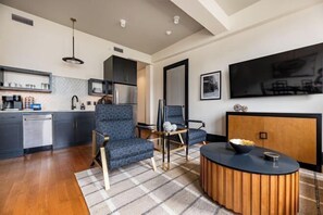 Un salon moderne comprenant un canapé, des fauteuils, une table basse et un coin cuisine avec des placards et des appareils électroménagers.