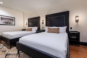 Une chambre d’hôtel avec deux lits, un grand tableau encadré au mur et un tapis à motifs.