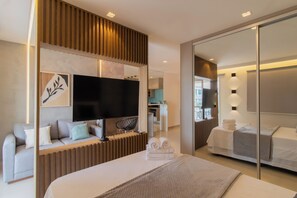A modern hotel room with a large bed, a flat-screen TV, a sofa, and a dining area. - Nook Studio 02.209 • Next to the store. Maya • Pool + Parking Lot (Guarulhos)