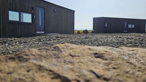 A modern building with a wooden exterior, large windows, and a gravel ground. - Hítarneskot – Private Hot Tub Cottage in Snæfellsnes (Borgarnes)