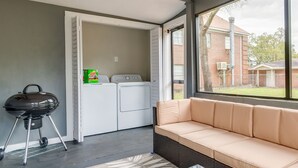 A laundry room with a washing machine and dryer, a barbecue grill, and a beige sofa in a room with a large window. - Pet-Friendly Pensacola Home Close to Beaches & Fun (Pensacola)