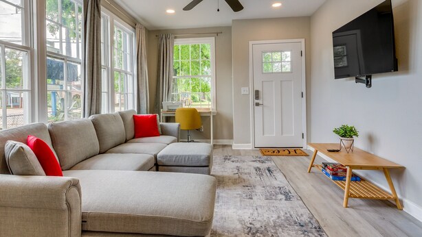 A modern living room with a sectional sofa, a ceiling fan, a flat-screen TV mounted on the wall, and a small wooden table with a plant. - Pet-Friendly Pensacola Home Close to Beaches & Fun (Pensacola)