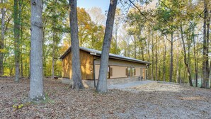 A cabin with a wooden exterior, surrounded by trees and a gravel driveway. - Cozy Couple’s Escape w/ Patio in Northwest Georgia (Calhoun)