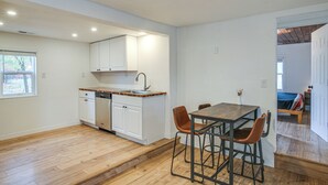 Eine moderne Küche mit weißen Schränken, einer Holzauskładung und einem Essbereich inklusive Holztisch und zwei Barhocker.