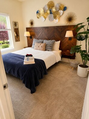 A bedroom with a herringbone-patterned headboard, a bed with a navy blue bedspread, two bedside lamps, and a potted plant.
