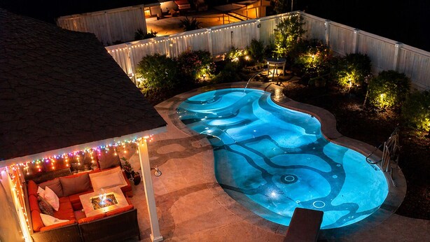 A swimming pool with a wavy design, surrounded by a patio area with a sofa and string lights. - The Oasis: Private 85° Pool + Bonus Shared Spa & Resort Garden
 (Kennewick)