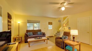 A living room with a brown sofa, a wooden coffee table, and a lamp. There is a staircase with a door at the top. - Riverside Serenity - Rivershire Retreat Guesthouse (Traverse City)
