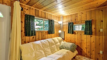 A wooden-paneled room with a bed, two windows with curtains, a lamp, and a door.