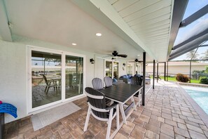 Eine Terrasse im Freien mit Tisch und Stühlen, einem Deckenventilator und Blick auf einen Swimmingpool.
