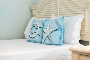 Ein Bett mit weißem Kopfteil, einem blauen Kopfkissen mit Meeresmotiven und weißer Bettwäsche.