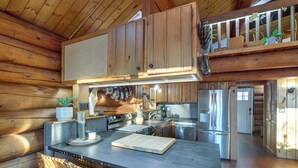 Interior de una cabaña de madera con cocina, que incluye una isla grande, armarios de madera y una lámpara colgante.