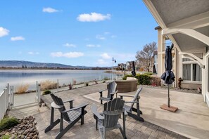 A patio with Adirondack chairs and a table overlooking a lake, with a building and a fence in the background. - SKI Home w/ Lake,City,MT Views • Resturants ,Shops,Casino's (Sparks)