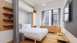 Ein modernes Schlafzimmer mit einem Bett, Holzregalen, einem Schreibtisch und einem Fenster mit Vorhängen.