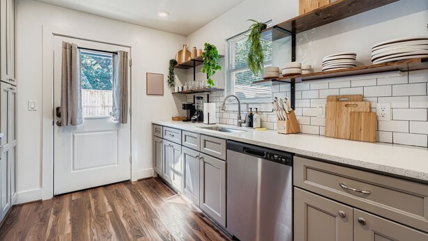 Una cocina moderna con armarios blancos, un lavavajillas de acero inoxidable y una encimera de madera.