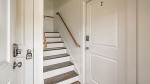 Una escalera de madera con peldaños y barandilla, que conduce a una puerta blanca con el número 2 en la parte superior.
