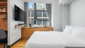 Une chambre d’hôtel moderne dotée d’un grand lit, d’un téléviseur à écran plat fixé au mur, d’un bureau en bois et d’une fenêtre donnant sur la ville.