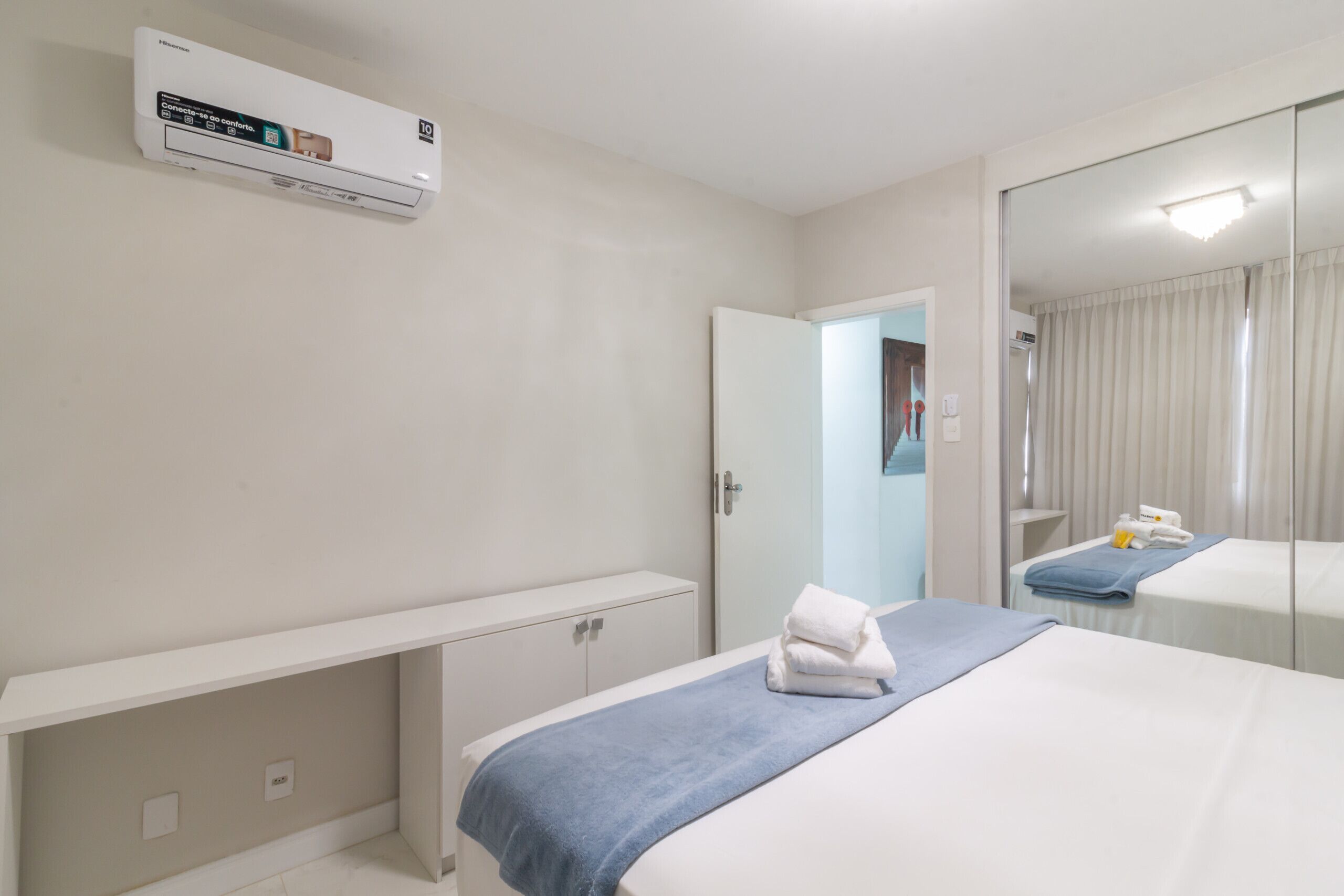 Una habitación de hotel con una cama, una mesita de noche, un espejo y un equipo de aire acondicionado.